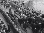Gustaf V:s kista i procession längs gator kantade av militärer och människor.