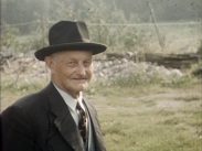 Halvbild av 77 årige Axel Andersson i kostym och hatt, hage i bakgrunden.
