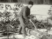 En skogsarbetare hanterar en yxa med en såg i förgrunden.