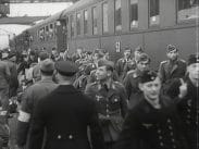 Uniformsklädda soldater på perrong. Tåg i bakgrunden, några soldater hänger ut ur fönstren.