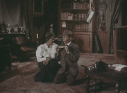 En kvinna i vit blus och en man utklädd till Sherlock Holmes i ett vardagsrum.
