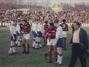 Två fotbollslag på plan inför en match, publik i bakgrunden.