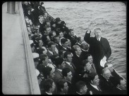 Ett femtiotal personer står på ett fartyg vid relingen och sjunger, körledaren syns i mitten av bilden med uppsträckt arm.