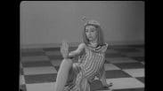 Birgit Cullberg som Kleopatra utför en pose under dansuppsättningen "Antonius och Kleopatra". Hon sitter på ett schackrutigt golv med höger arm utsträckt och handen vinklad uppåt.