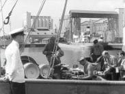 En handfull män äter på ett fartyg vid kajen, Trelleborgs hamn i bakgrunden.