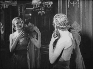 Kvinnlig mannekäng framför spegel iklädd 1930-talsutstyrsel med rosett på höger axel.
