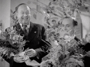 Stillbild ur journalfilmen Veckorevy 1943-02-08 med skådespelarna Thor Modéen och Åke Söderblom som håller varsin blombukett.