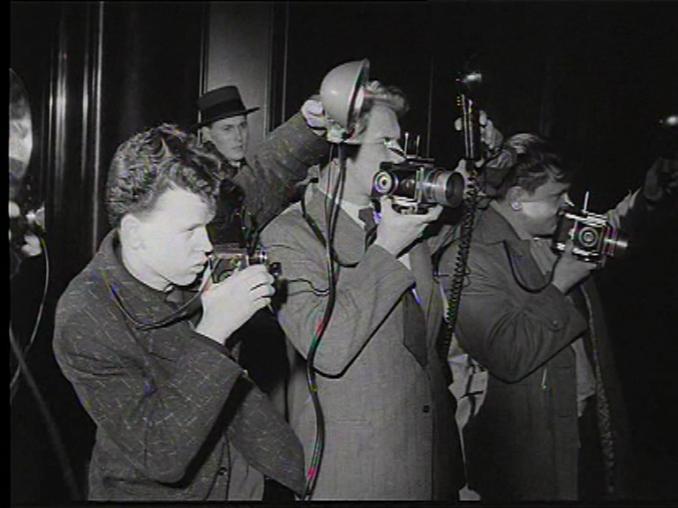 Tre pressfotografer med äldre stillbildskameror med separata blixtar.